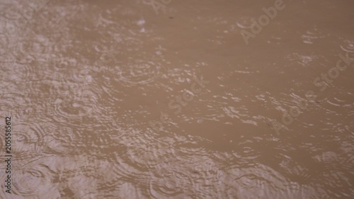 Close-up of raindrops falling on muddy brown water, creating circular ripples and splashes during a storm, illustrating the impact of heavy rainfall.