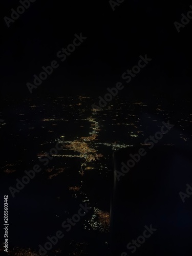 Spectacular aerial night view from an airplane window showing glowing city lights far below. Urban landscape illuminated in darkness, capturing travel, aviation, and the beauty of a city at night.