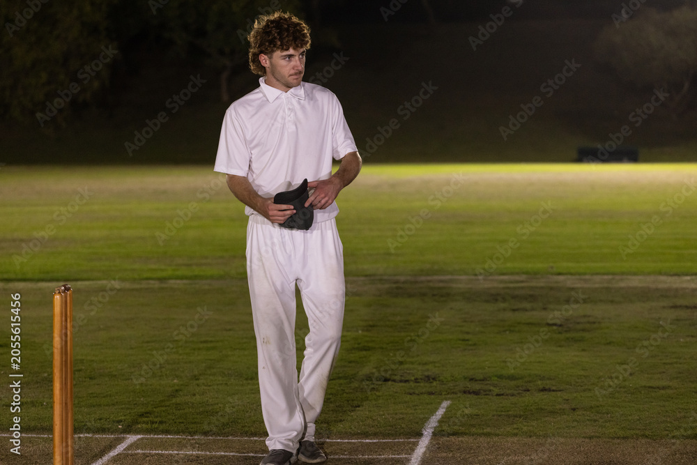Obraz premium Wooden cricket stumps are standing on pitch at night with dark cap and floodlights casting glow