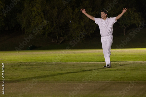 Obraz na plátně Man in white uniform and athletic shoes raising arms on lit pitch under floodlig