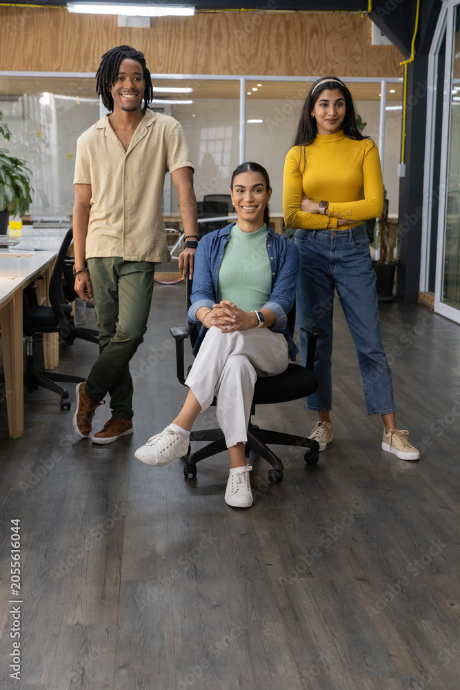 Fototapeta premium Diverse coworkers posing in modern open-plan office, seated woman center with swivel chair