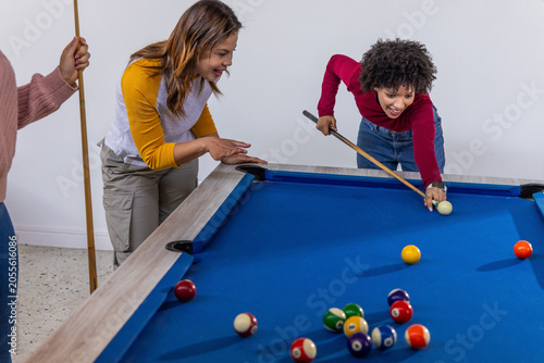 Diverse friends playing pool, woman lining shot on pool table with cue, scattered balls, copy space