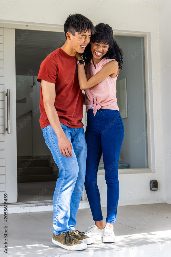 Obraz premium Diverse couple laughing and leaning after opening door at home entry, celebrating arrival in jeans