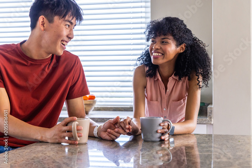 Vertical video: Light through blinds leading couple clasping hands and sharing mugs at kitchen bar