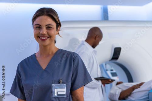 Fotografie Smiling African American woman in gray scrubs showing badge, colleague using sca