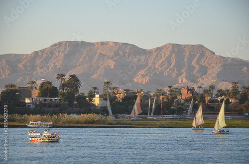 Obraz na plátne Traditional felucca sailboats and motorboats sailing on the Nile River against the backdrop of the West Bank mountains in Luxor, Egypt during golden hour