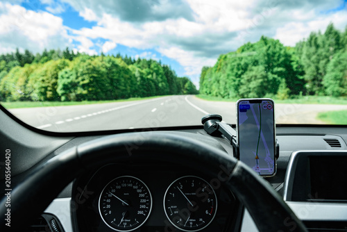 Smartphone with navigation route on screen mounted on phone holder at car dashboard.