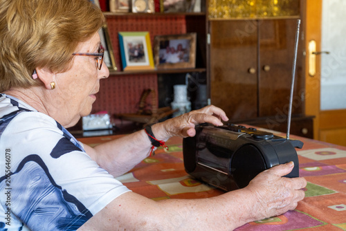 Senior woman listening to a cassette on a vintage radio cassette player at home
