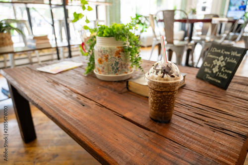 Close up of an iced coffee with whipped cream and chocolate drizzle on a wooden table at an outdoor cafe.