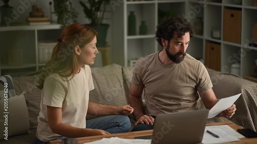 Stressed couple arguing about financial problems, debts, and unpaid bills while managing home budget with a laptop at night