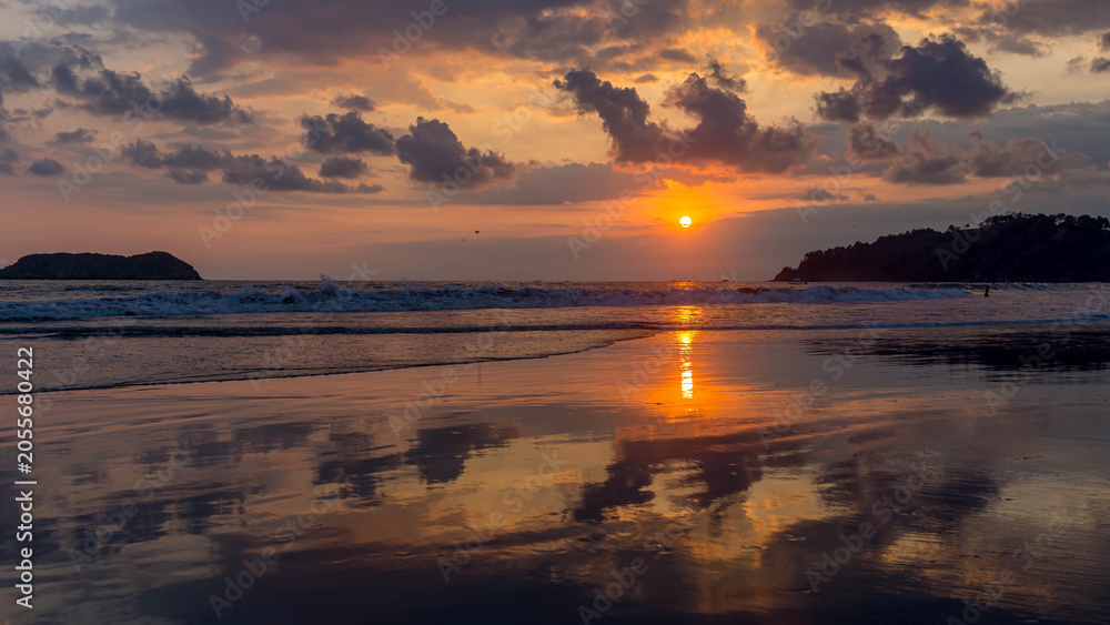 Obraz premium Vivid sunset over ocean waves reflecting on wet sand at tropical beach in Costa Rica