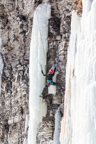 Foto Ice climber ascending a frozen waterfall on a rocky cliff using ice axes and cra