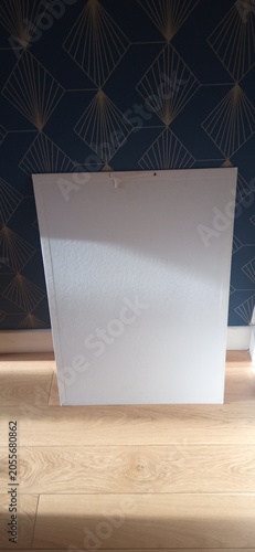 Schilderij op canvas Blank white canvas leaning against geometric wallpaper on wooden floor