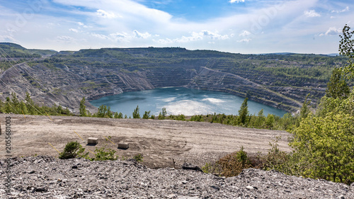 Aerial view of a flooded open pit mine surrounded by terraced rock walls and greenery