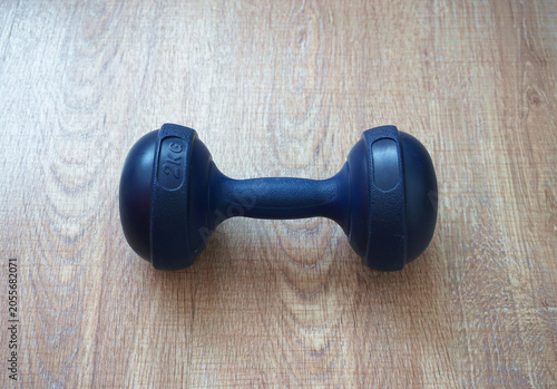 Single blue 2kg dumbbell on a wooden floor background. Vinyl coated hand weight for fitness, aerobic and home gym exercise. Sport equipment object for healthy lifestyle and physical training concept. 