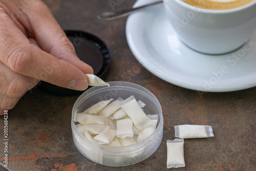 Photos man holding white nicotine pouch or snus portion in fingers and a cup of coffee