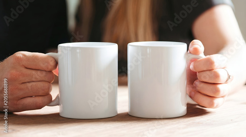 Two blank white ceramic mugs in a cozy setting, a perfect mockup for showcasing your designs