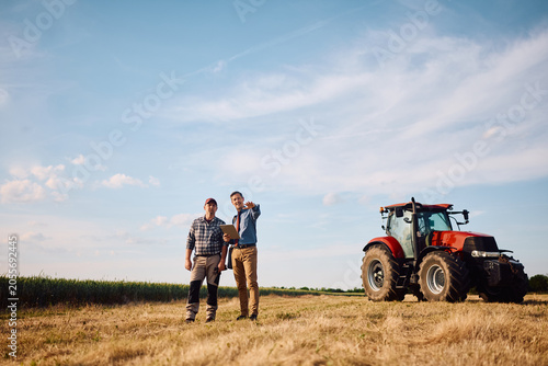Full length of insurance advisor and farmer inspecting field.