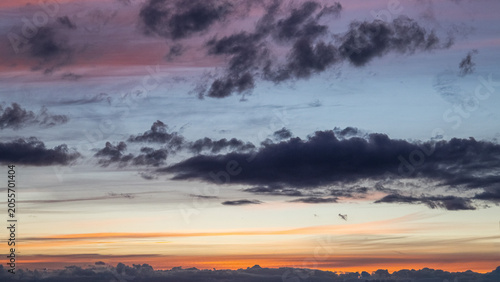 Beautiful pastel sunset sky filled with dramatic dark clouds and soft orange, pink and blue tones near the horizon. Atmospheric evening landscape showcasing colorful cloud formations and tranquil twil