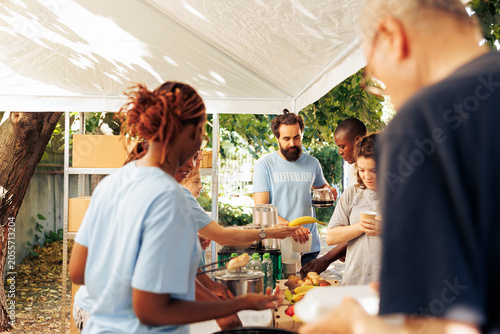 Slika na platnu On sunny day, group of volunteers at local food bank handing out free food to the underprivileged homeless people outdoors, humanitarian aid team providing meals and non-perishable items to the needy