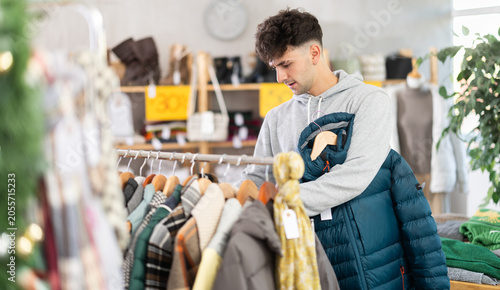 Foto Selective young guy choosing down jacket in clothing shop with large collection