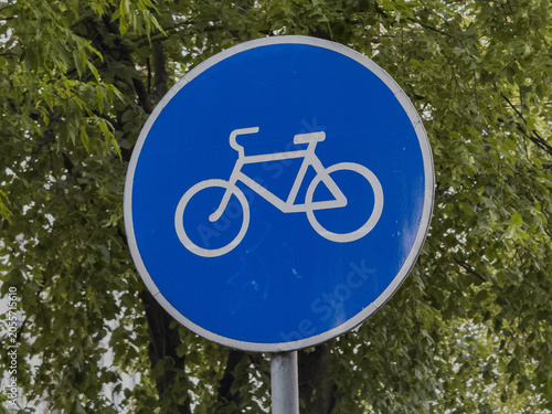 Obraz na płótnie Blue round bicycle lane road sign on pole against green tree foliage outdoors, u