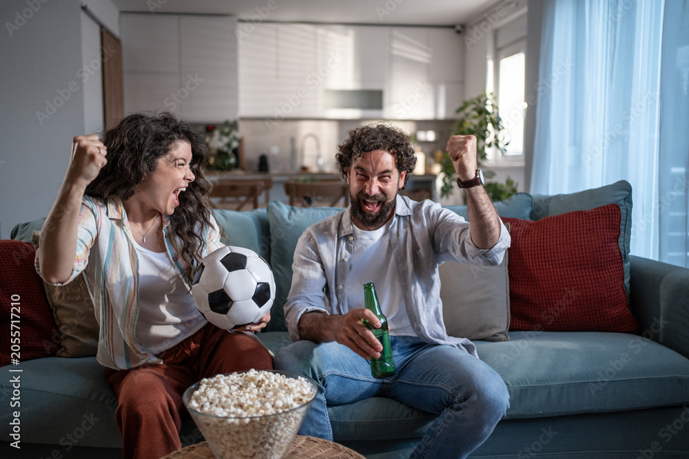 Naklejka premium Young couple celebrating sports victory watching soccer on tv