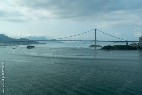Suspension bridge over calm water with boats and cloudy sky in coastal city landscape