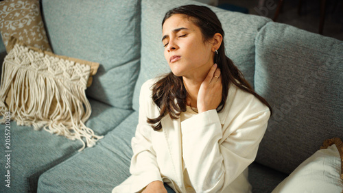 Schilderij op canvas Young Hispanic woman sitting on her sofa at home after work suffering from severe neck muscle tension