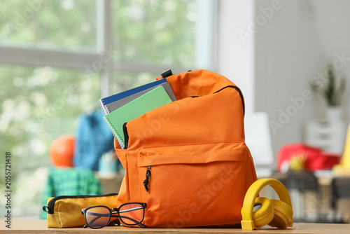 Tableau sur toile Orange backpack with school supplies, notebooks, glasses, and headphones on wood