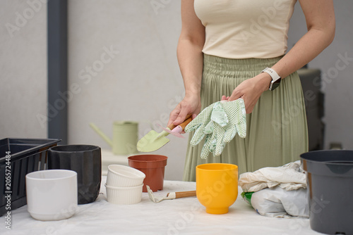 Schilderij op canvas Woman prepares pots and gardening tools at work table, holding gloves and a hand