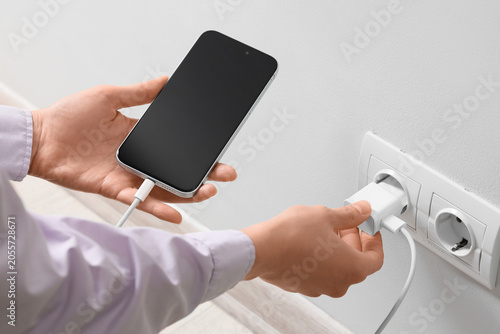 Принти на полотні Person plugging smartphone charger into wall outlet for mobile device power and