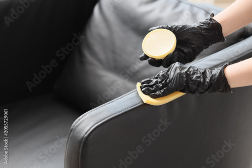 Fotografie Female hands polishing black leather armchair, closeup
