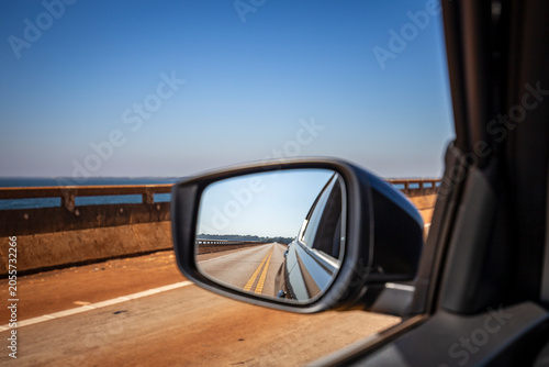 Car side mirror reflection on open highway bridge