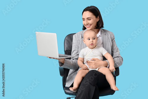 Working mother with her baby and laptop in chair on blue background