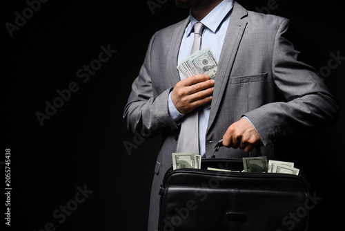 Obraz na plátne Businessman in gray suit hiding US dollar banknotes in jacket pocket and briefca