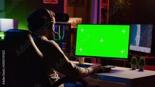 Fotografía Man in dimly lit apartment playing video games on green screen gaming PC at computer desk, enjoying day off from work