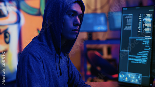 Tableau sur toile Asian hacker in dark hidden shelter trying to launch DDoS attack on website by sending large amounts of traffic from multiple sources to overwhelm IT