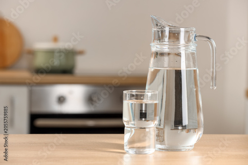 Foto Clear glass pitcher and tumbler filled with fresh drinking water on a wooden kit