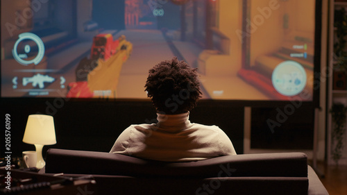 Foto African American man playing singleplayer videogames on widescreen TV, relaxing after long day at work, gamer enjoying science fiction first person shooter game on gaming console, having fun