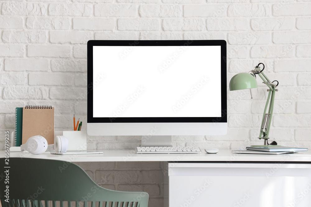 Fototapeta premium Modern home office workspace with blank computer screen, white brick wall background, and minimalist desk setup