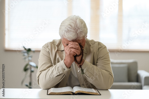 Photos Elderly man praying with rosary beads and open bible, spiritual devotion and rel