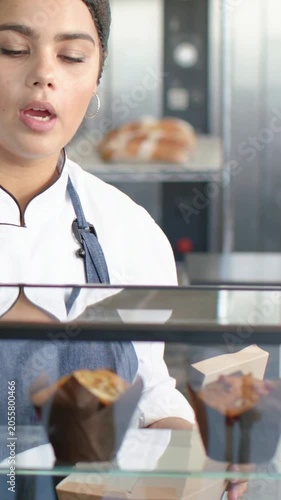 Vertical video: Customer pointing chef in coat placing muffin in box with tongs at shop, copy space