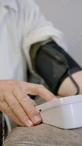 Vertical video: Adjusting senior securing black cuff in robe at home after monitor set, checking BP