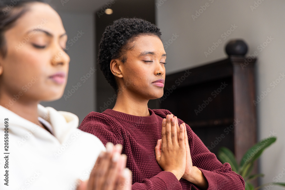 Obraz premium Indian, African American women meditating with hands in prayer at home, maroon sweater white hoodie