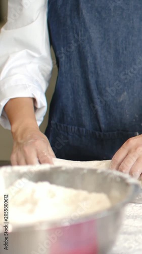 Vertical video: Pressing dough, baker in denim apron shaping portions on floured counter for baking