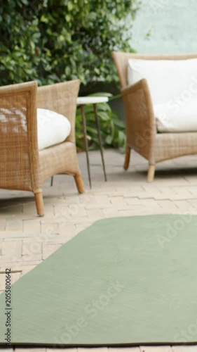 Vertical video: Tilting camera revealing green yoga mat on patio for yoga with wicker chairs, pool