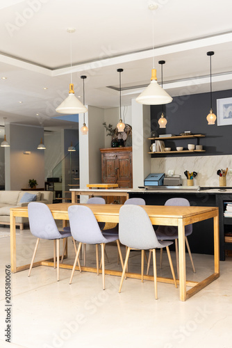 Modern open-plan dining room featuring rectangular wood table, six grey chairs, pendant lights