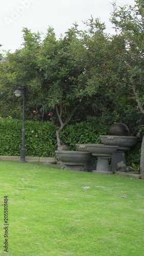 Vertical video: Panning camera revealing tiered stone fountain on lawn, showing lamppost and hedge