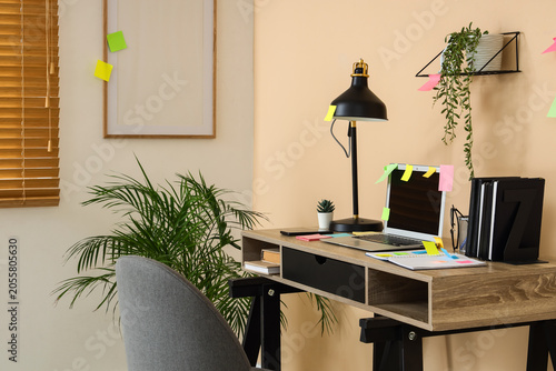 Workplace with laptop, lamp and sticky notes in office interior